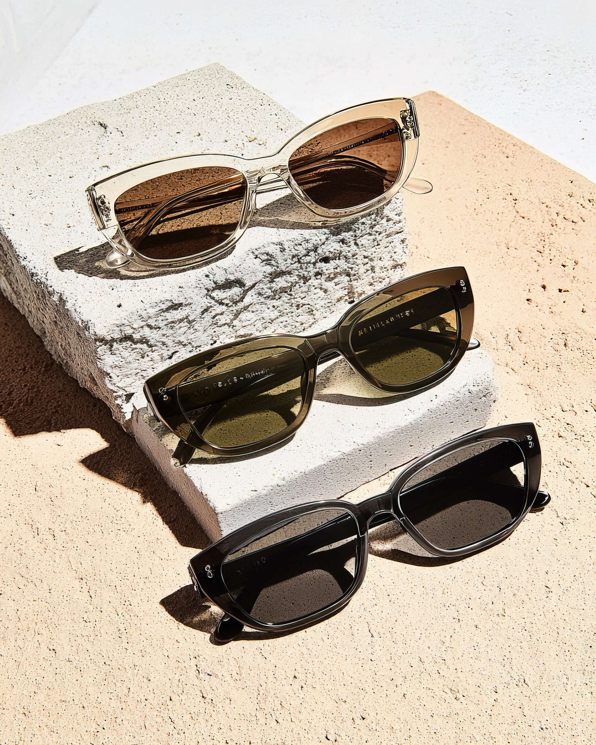 Three stylish sunglasses on concrete showcasing photophobia protective lenses in various tints and styles.